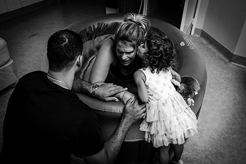 Pregnant lady in a birthing pool surrounded by toddler and husband